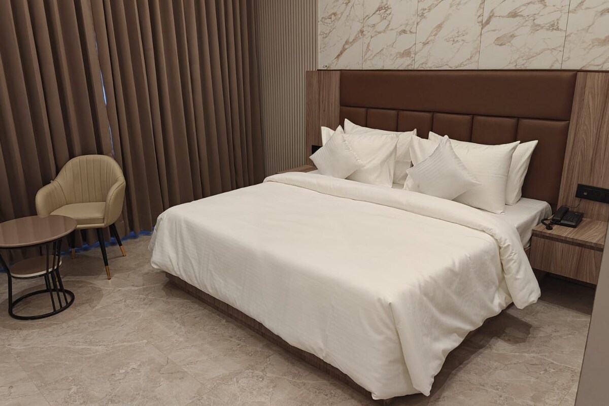 Une chambre d’hôtel avec un grand lit, une petite table ronde, deux chaises et une table de chevet en bois avec un téléphone.