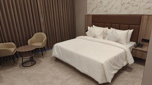 Une chambre d’hôtel avec un grand lit, une petite table ronde, deux chaises et une table de chevet en bois avec un téléphone.