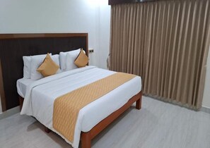 Een hotelkamer met een bed, gordijnen en een houten hoofdeinde.