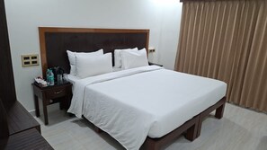 Een net opgemaakt bed met witte lakens, een houten hoofdbord en een nachtkastje met een lamp en een fles water.