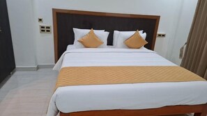 Een hotelkamer met een groot bed, twee kussens, een houten hoofdbord en een beige sprei.