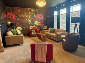 Ein Wohnzimmer mit floralem Wandbild, einem roten Sessel, einem beigen Sofa und einem Ledersessel in Dunkelbraun.