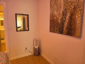 Een kamer met een bed, een spiegel, een luchtzuiveraar aan de muur en een groot abstract schilderij.