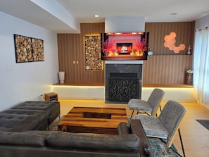 Een moderne woonkamer met een open haard, een flatscreen televisie en een zithoek met een salontafel.