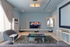 Uma sala de estar moderna com televisão de tela plana, sofá, mesa de centro e uma janela grande com cortinas.