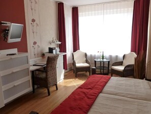 Ett hotellrum med en säng, två stolar, ett skrivbord, en tv och ett fönster med gardiner.