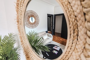 A living room with a round mirror, a sofa, a coffee table with magazines, and a potted plant. - New Listing (Reims)