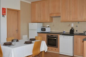 Kompakti keittiö, jossa on puukalusteet, jääkaappi, mikroaaltouuni, uuni ja astianpesukone.