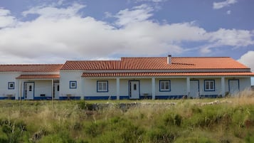 Une rangée de bâtiments à deux étages, avec des toits recouverts de tuiles rouges et des murs blancs, entourés de champs verdoyants.