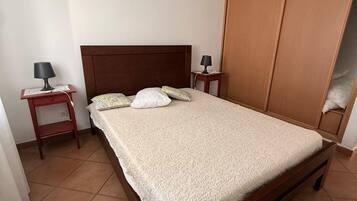 Une chambre à coucher avec un lit en bois, deux tables de chevet, un luminaire suspendu et une armoire.