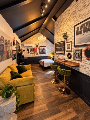 A loft-style bedroom with a sloped ceiling, a bed, a yellow sofa, and a dining area with a bar. - Eclectic Tiny Home, Private Hot Tub, Shared Pool, In Between Beach & Downtown (Wilmington)