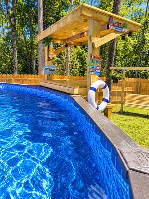 A swimming pool with a wooden deck area, a lifebuoy, and a sign for a tiki bar. - Eclectic Tiny Home, Private Hot Tub, Shared Pool, In Between Beach & Downtown (Wilmington)
