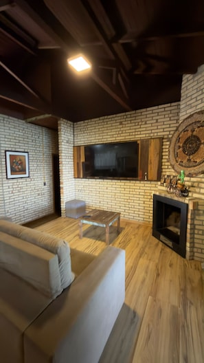 Ein Wohnzimmer mit Backsteinwand, Flachbildfernseher, Sofa und Kamin.