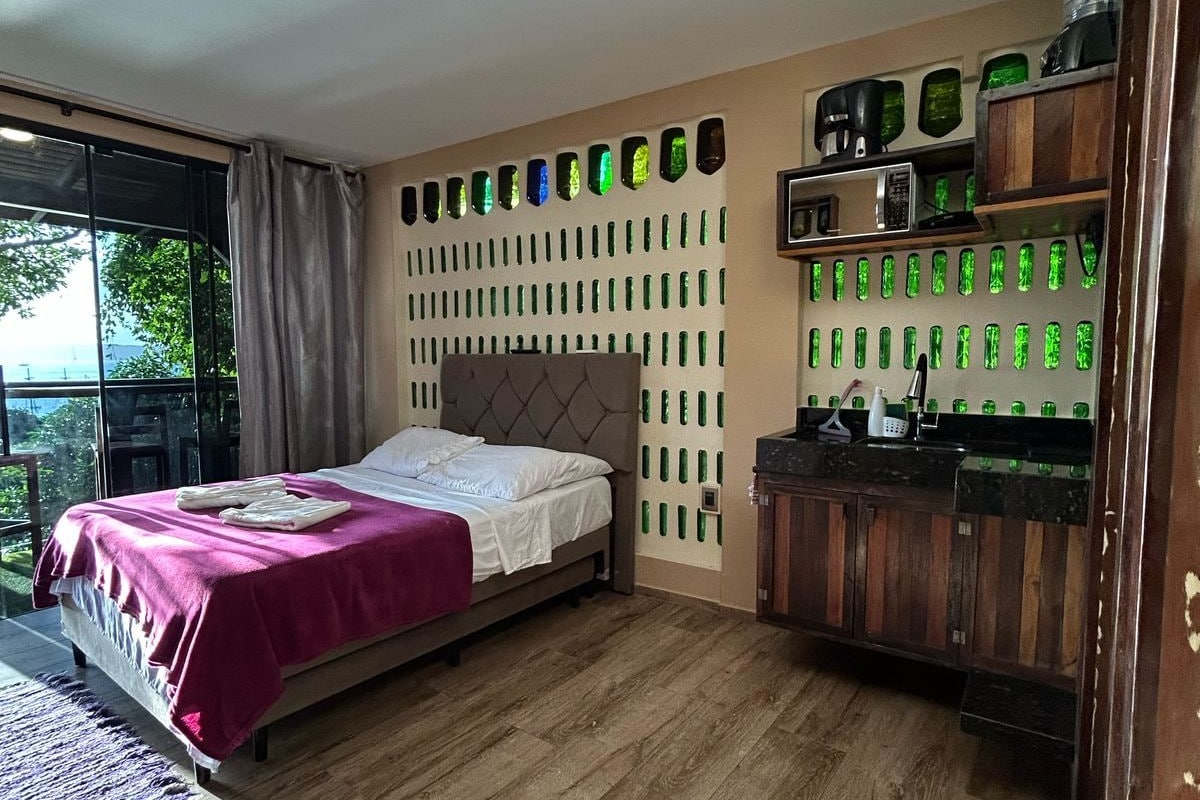 Ein Schlafzimmer mit einem Bett, Holzboden, einem Fenster mit Vorhängen und einer Wand mit grünen, flaschenförmigen Dekorationen.