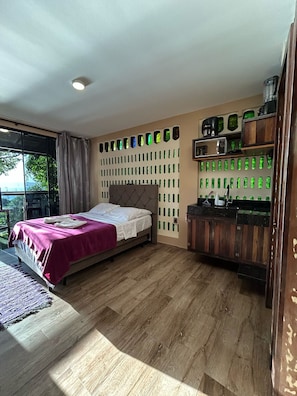 Ein Schlafzimmer mit einem Bett, Holzboden, einem Fenster mit Vorhängen und einer Wand mit grünen, flaschenförmigen Dekorationen.
