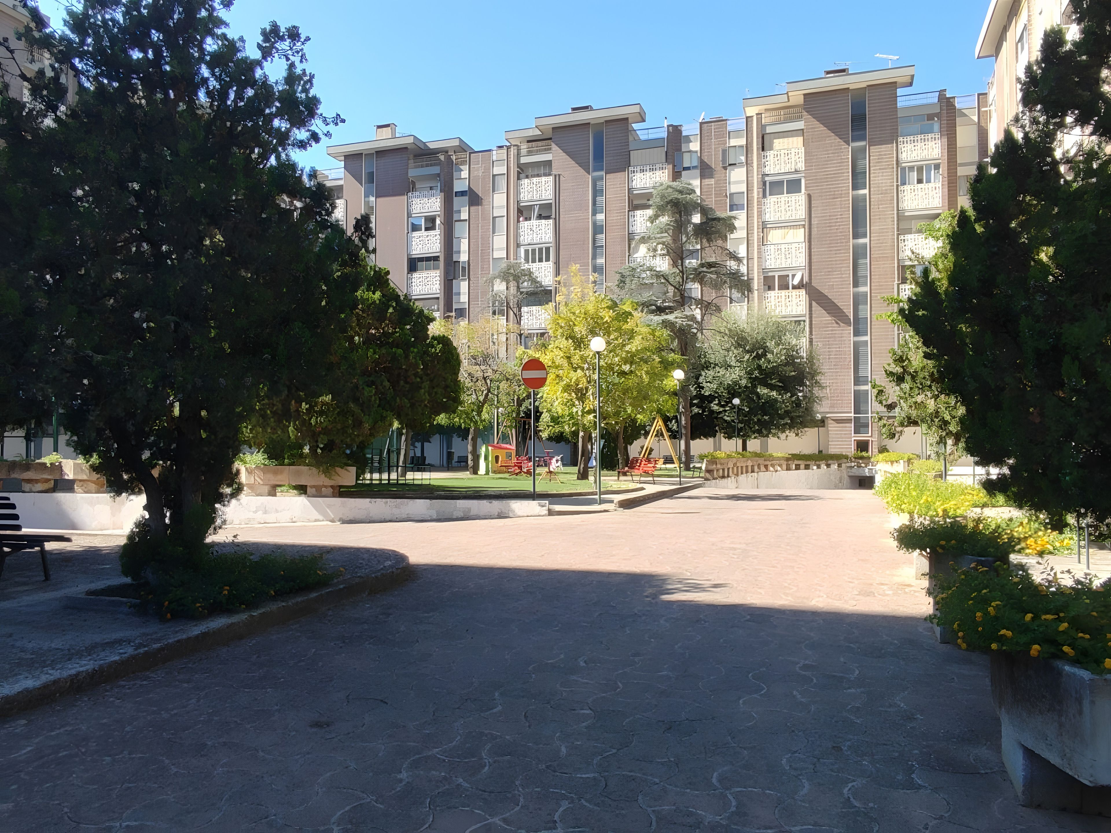 A residential area with apartment buildings, a playground, and a paved courtyard.