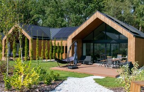 A modern house with a large glass window, a patio with outdoor furniture, and a hammock. - Cozy home in Lawica with sauna (Lawica)