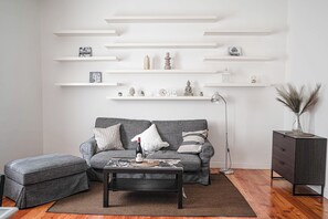 A living room with a grey sofa, a coffee table, and a bookshelf with various decorative items. - New Listing (Roma)
