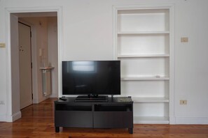 Un televisor sobre un soporte negro en una habitación con paredes blancas y suelo de madera.