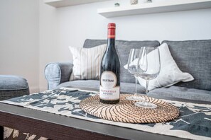 Una botella de vino Bertani Valpolicella Ripasso sobre un camino tejido en una mesa, con una copa a su lado, en una sala de estar con un sofá gris y almohadones a rayas.