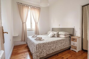 A bedroom with a bed, a nightstand, a lamp, and a window with curtains. - New Listing (Roma)