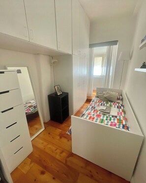 Un dormitorio pequeño con cama, mesita de noche, armario y espejo.