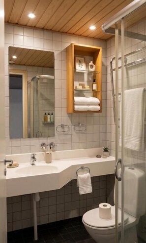 A modern bathroom with a glass shower enclosure, a white sink with a wooden vanity, and a toilet with a roll of toilet paper. - Tiera Resort (Taivalkoski)
