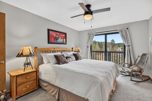 A bedroom with a bed, bedside tables, a ceiling fan, a window with curtains, and a view of the outdoors. - Ski-In Breck Getaway | Community Hot Tub; Downtown Access (Breckenridge)
