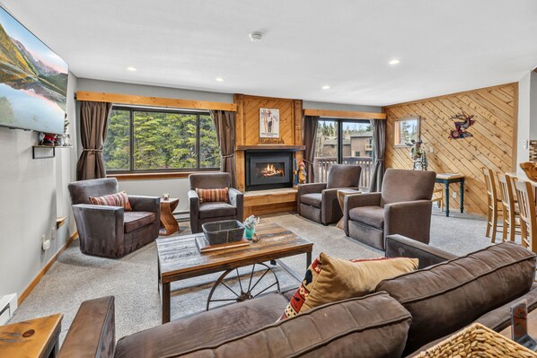 A cozy living room with a fireplace, comfortable seating, and large windows offering a view of the outdoors. - Ski-In Breck Getaway | Community Hot Tub; Downtown Access (Breckenridge)