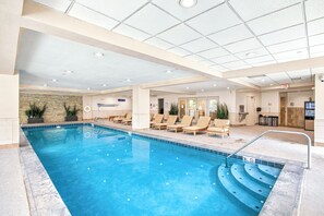 An indoor swimming pool with lounge chairs and a stone wall. - New Remodel Penthouse by InvitedHome | Walk to Ski/Town, Hot Tub, Pool, Gym (Beaver Creek)
