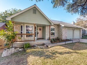 A single-story house with a front porch, a garage, and a stone exterior. - Newly Remodeled Western 3BR House With Cowboy Pool - Quiet and Great Location (Austin)