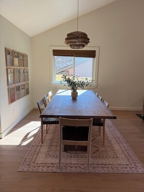 A dining room with a long wooden table, chairs, a hanging light fixture, a window with blinds, and a patterned rug. - Newly Remodeled Western 3BR House With Cowboy Pool - Quiet and Great Location (Austin)