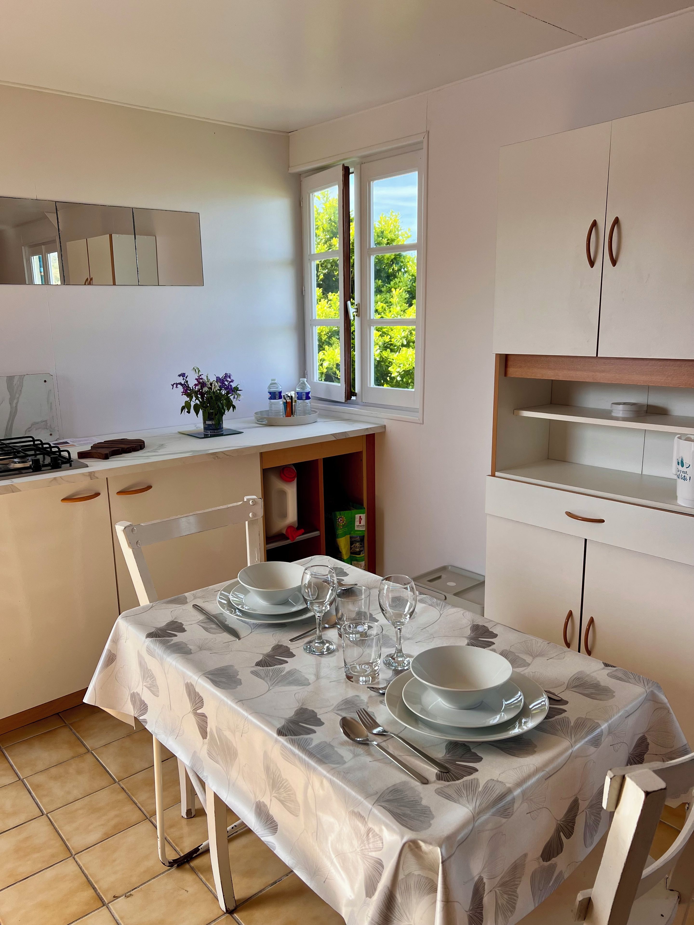 A kitchen with a dining table set for four, a window with a view of greenery, and cabinets with wooden handles.