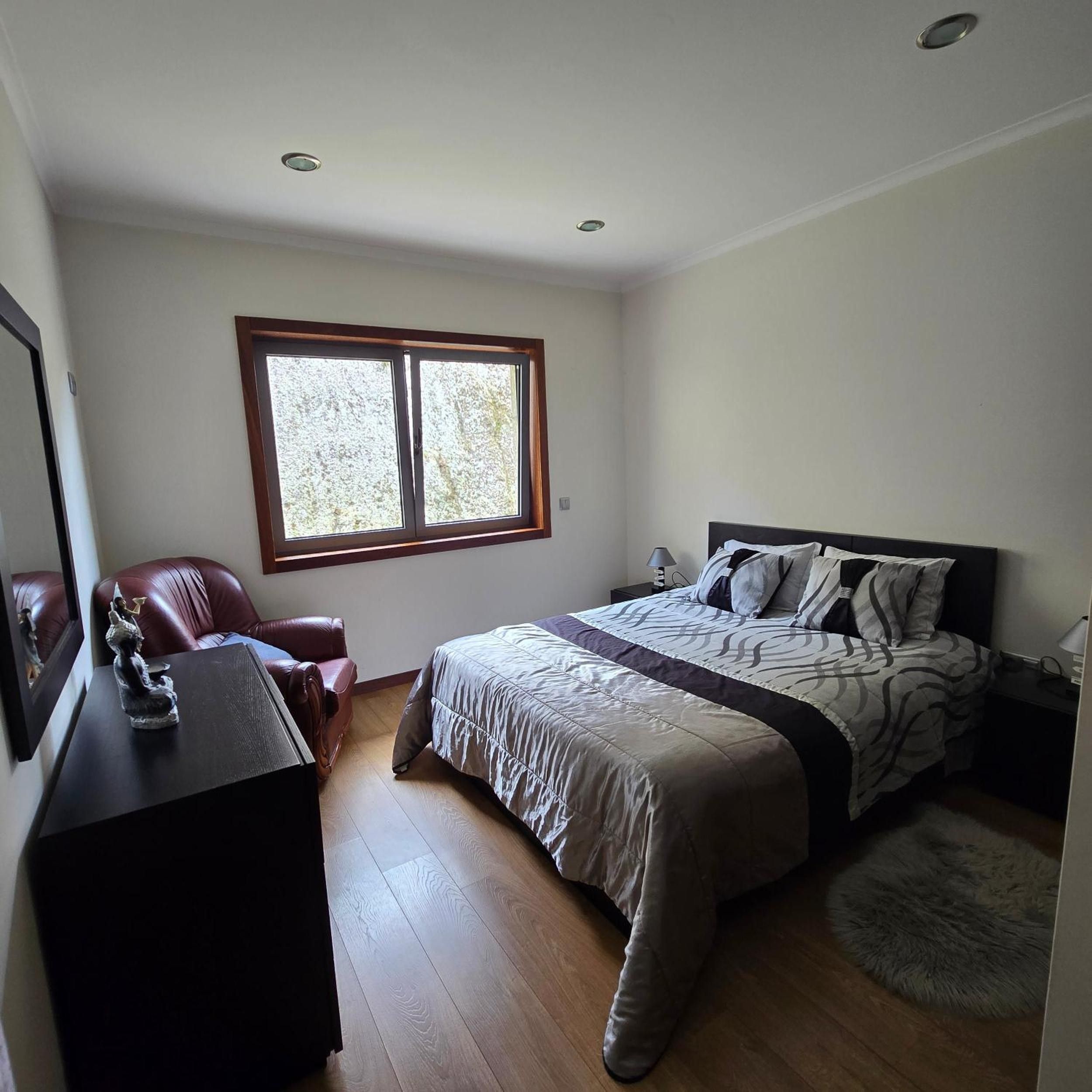 Un dormitorio con cama, escritorio, silla, ventana y mesita de noche.