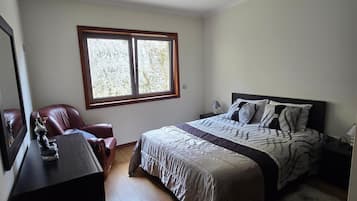 Un dormitorio con cama, escritorio, silla, ventana y mesita de noche.