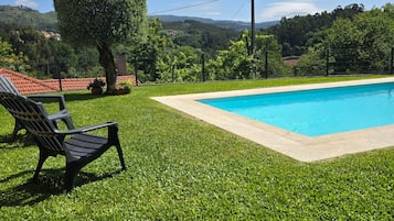 Una piscina con un área verde alrededor, una banca y vistas al campo.