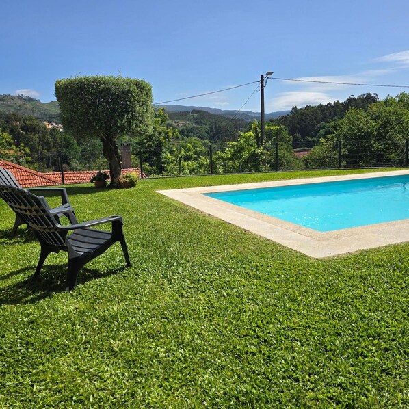 Une piscine entourée d’une pelouse, avec un banc et une vue sur la campagne.