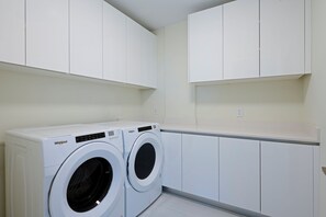 A laundry room with two white Whirlpool washing machines, white cabinets, and a white countertop. - Luxury Beachfront Fully Furnished Penthouse PPH2 in Singer Island!! (Riviera Beach)