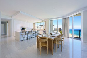 A modern kitchen with white cabinets, a dining area with a large table and chairs, and a view of the ocean. - Luxury Beachfront Fully Furnished Penthouse PPH2 in Singer Island!! (Riviera Beach)
