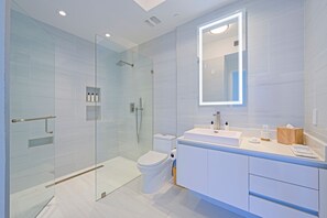 A modern bathroom with a glass shower enclosure, a toilet, and a vanity with a mirror. - Luxury Beachfront Fully Furnished Penthouse PPH2 in Singer Island!! (Riviera Beach)