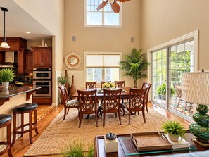Un comedor espacioso con una mesa y sillas de madera, una cocina con electrodomésticos modernos y grandes ventanales con vistas al exterior.