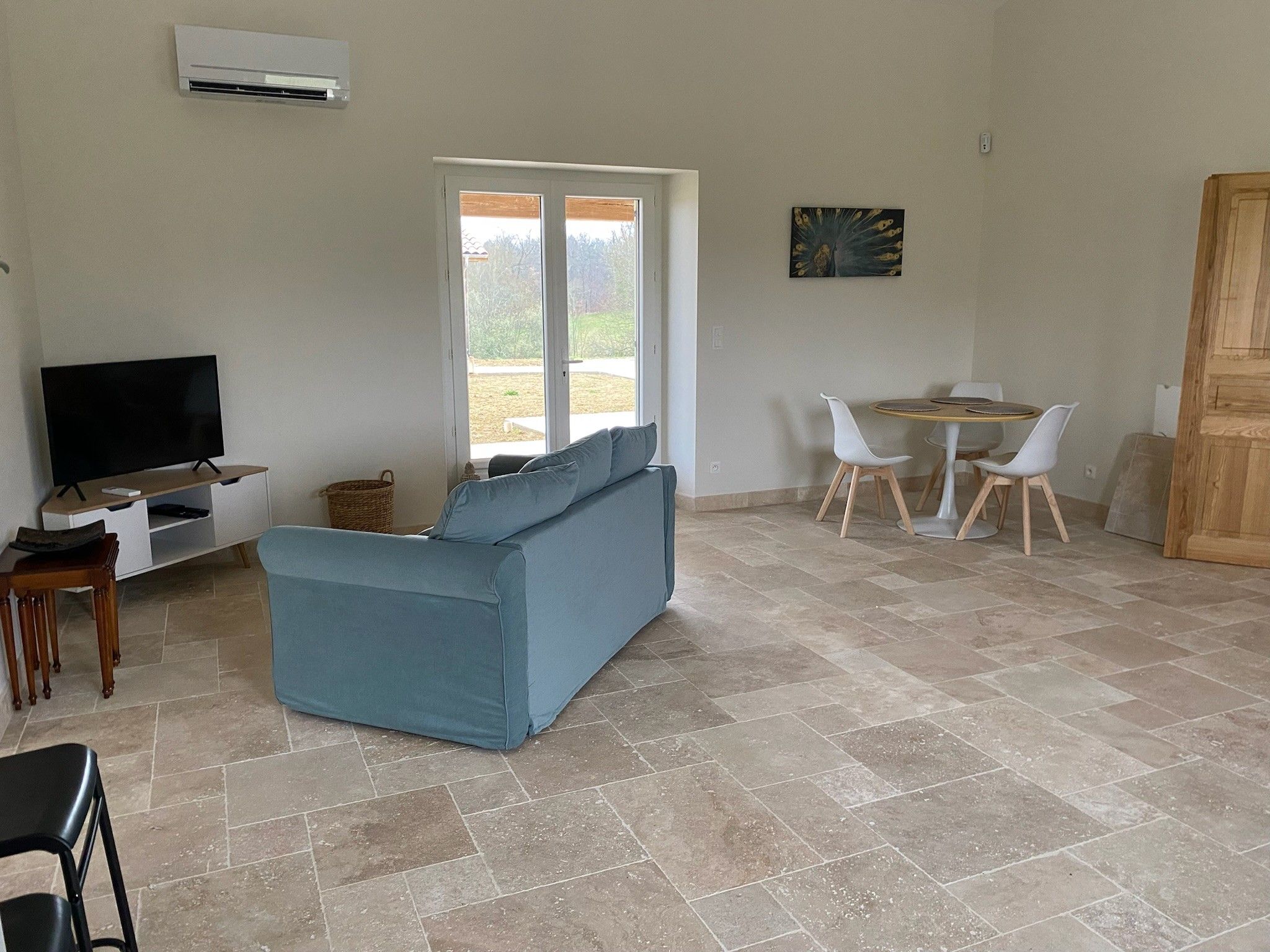Una sala de estar con sofá, televisor, zona de comedor con sillas y un ventanal grande.