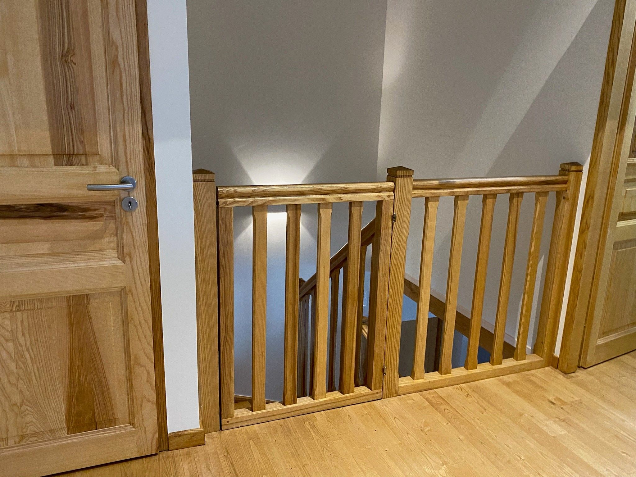 Una escalera de madera con barandilla y una puerta a la izquierda.