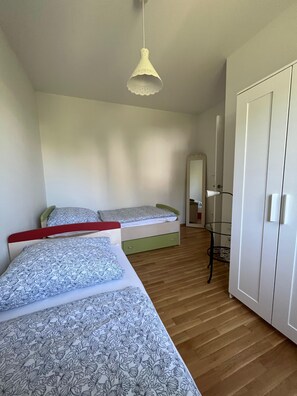 Ein Schlafzimmer mit zwei Betten, einem Kleiderschrank, einem Spiegel und einer Deckenleuchte.