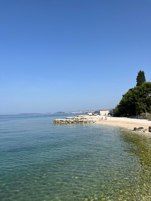 Klarer Küstenblick mit felsiger Küstenlinie, Sandstrand und einigen Gebäuden im Hintergrund.