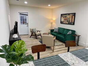 Un salon avec un canapé vert, deux fauteuils, une table basse, une lampe et un tableau au mur.