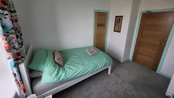 A single bed with a green bedspread, a pillow, and a folded towel. There are two doors, one with a mirror above it, and a radiator on the floor.