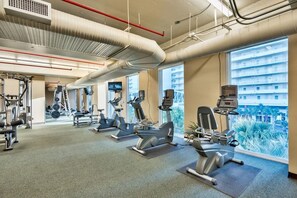 Una palestra con diverse attrezzature per esercizi, ampie finestre e vista su un edificio esterno.