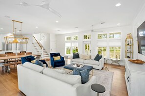 A spacious living area with a white sofa, blue armchair, and a dining table. - 🏖️ Caspian Blue Cottage | Beach Access, Pool, Bikes & Screened Porches 🚲 (Inlet Beach)