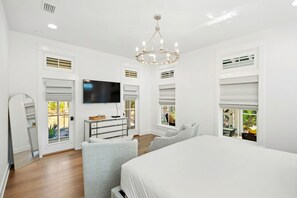 A bedroom with a large bed, a TV mounted on the wall, and a chandelier. - 🏖️ Caspian Blue Cottage | Beach Access, Pool, Bikes & Screened Porches 🚲 (Inlet Beach)